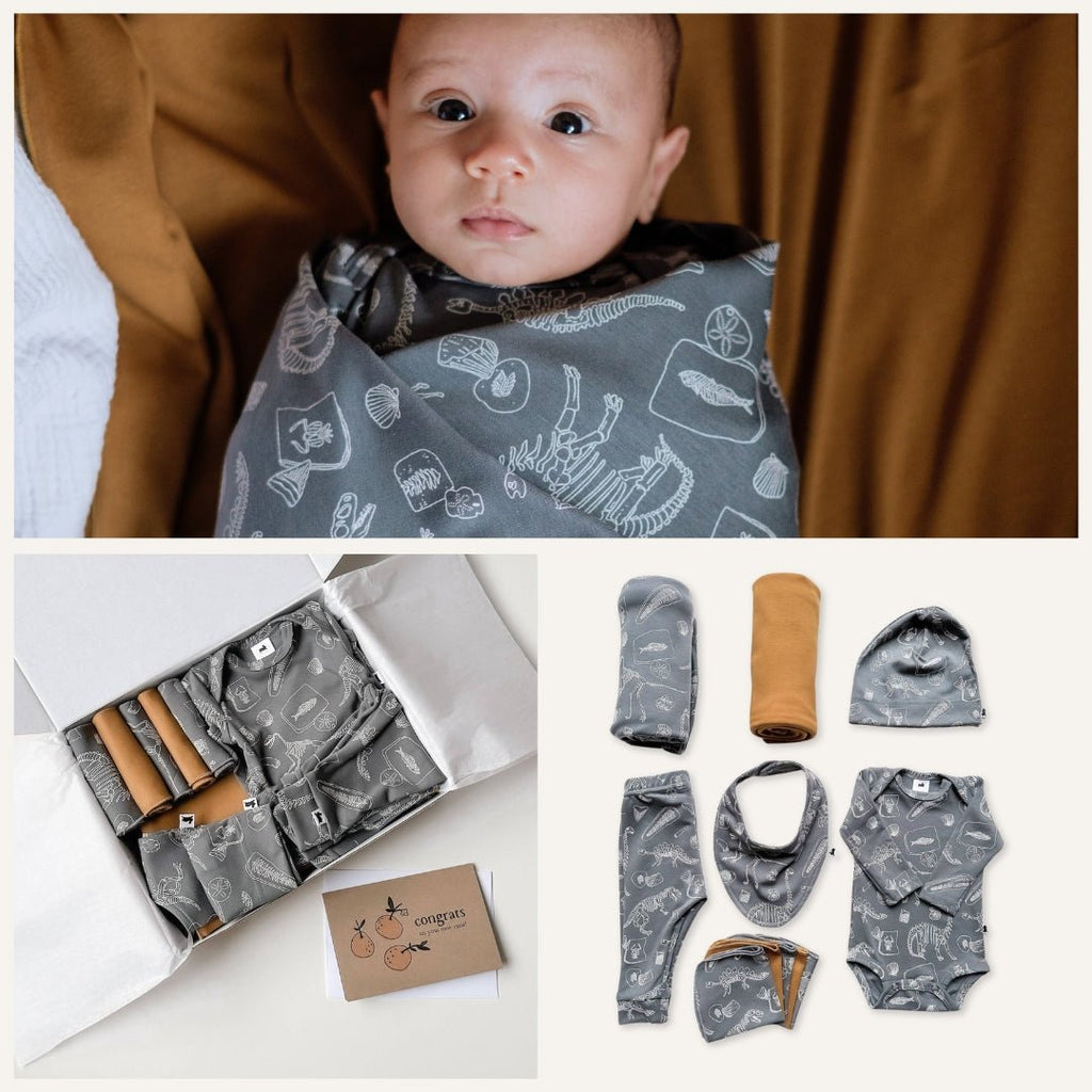 Baby wearing a gray bib with animal patterns, surrounded by baby clothes and accessories on a white background.